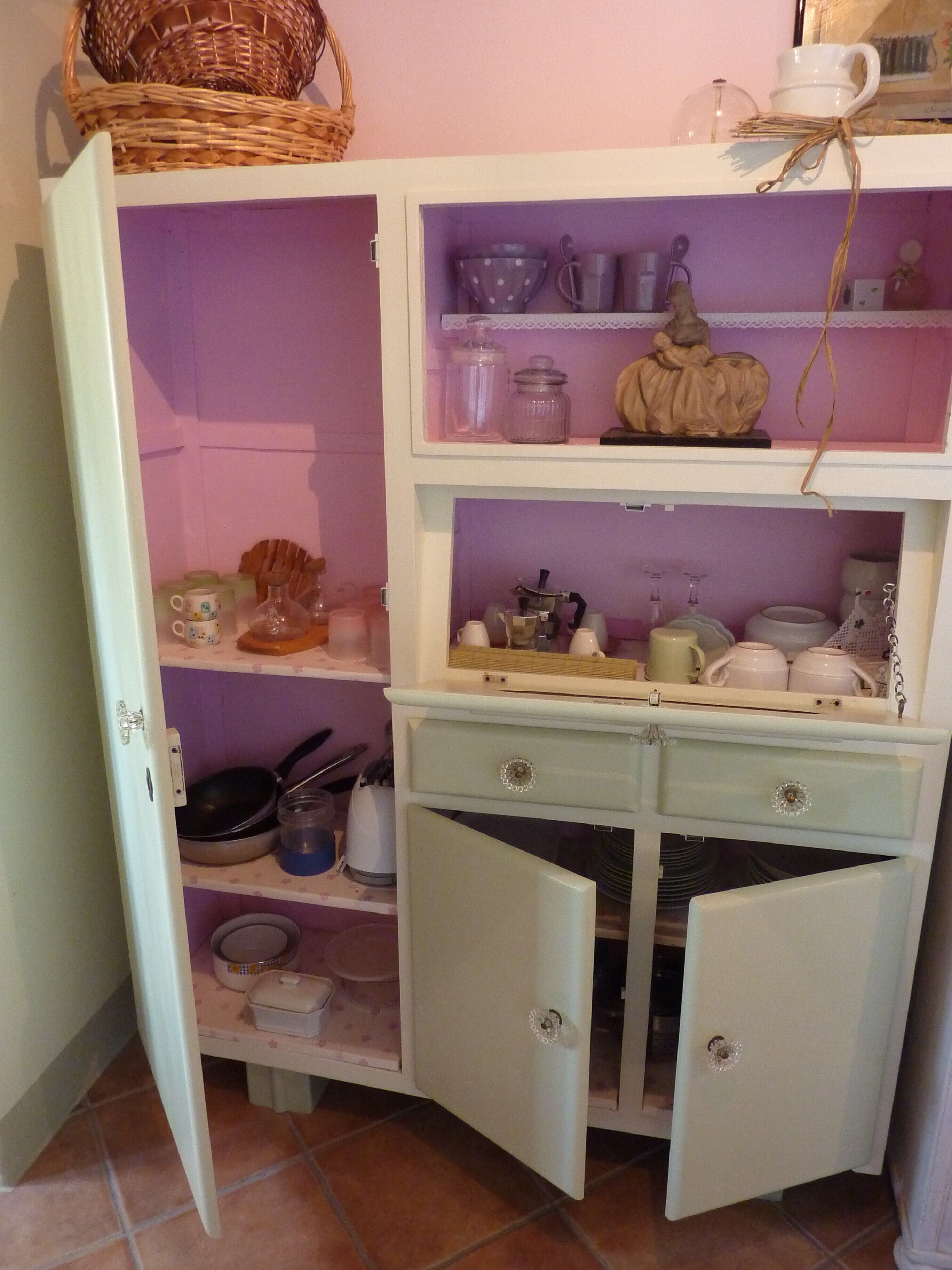 A kitchen with open cabinets, shelves with kitchenware, and a basket on the top shelf.