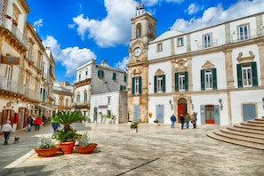 A historic square with buildings, a clock tower, and potted plants.