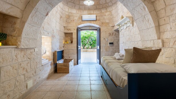 Una habitación pequeña con paredes de piedra, una cama, una mesita y un televisor.