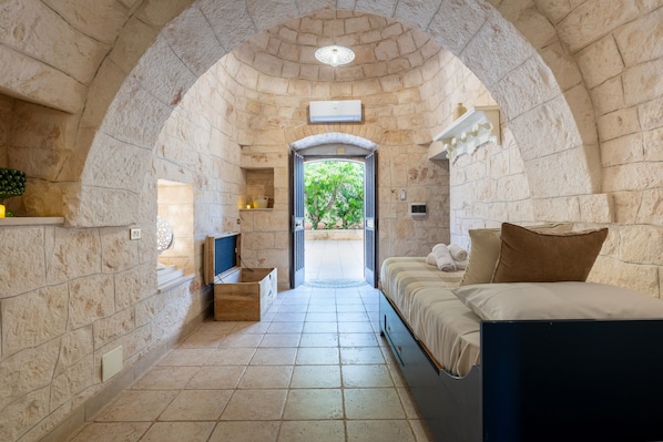 A narrow stone-walled room with a bed, a small table, and a television.