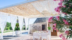 Un patio al aire libre con mesas y sillas blancas, un muro de piedra y una puerta de madera.