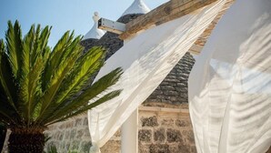 Un edificio de piedra con techo abovedado blanco, una palmera y tela blanca cubriendo una estructura.