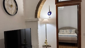 Een moderne woonkamer met een flatscreen-tv, een decoratieve lamp en een bed op de achtergrond.