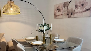 Een eetruimte met een glazen tafel, gestoffeerde grijze stoelen en een hanglamp.