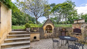 Un patio de piedra con horno de ladrillo, asientos al aire libre y una escalera que lleva a una puerta.