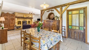 Un área de comedor con una mesa, sillas, un florero con flores, un armario de madera y una ventana con vidrieras.