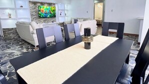 A dining area with a long table, chairs, and a central decorative item. There are sofas and a TV in the background. - Luxury & Location, Beautiful & Spacious Apt in Altamira (Caracas)