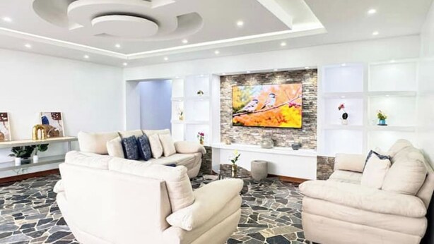 A modern living room with a stone floor, a white sofa, a white armchair, and a flat-screen TV mounted on a stone wall. - Luxury & Location, Beautiful & Spacious Apt in Altamira (Caracas)