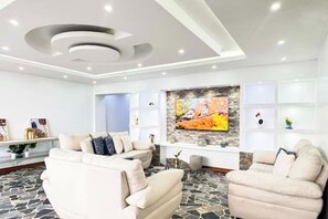 Ein modernes Wohnzimmer mit Steinboden, einem weißen Sofa, einem weißen Sessel und einem Flachbildfernseher, der an einer Steinsäule angebracht ist.