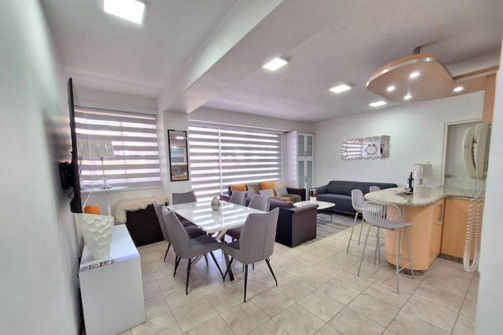 Un salon moderne comprenant un coin repas, un canapé, un téléviseur et une cuisine avec un bar.