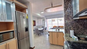 A modern kitchen with stainless steel appliances, a dining area with a table and chairs, and a view of the outside through large windows. - Luxury & Location, Beautiful Apartment in Los2Caminos-Boleita (Caracas)