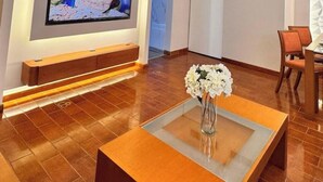 Un vestíbulo moderno con un banco de madera, una mesa de centro de vidrio y un jarrón de flores, y un televisor de pantalla plana montado en la pared.