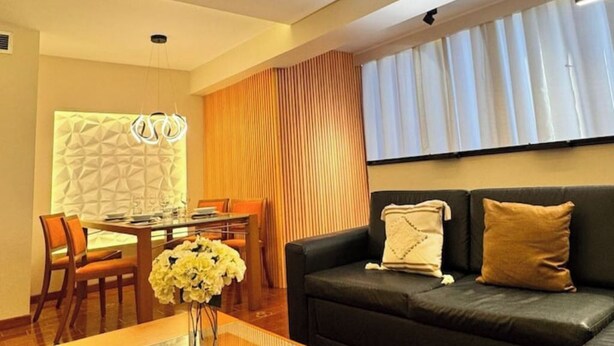 Una sala de estar moderna con un sofá de cuero negro, una mesa de centro de vidrio y un comedor con sillas y una mesa de madera.