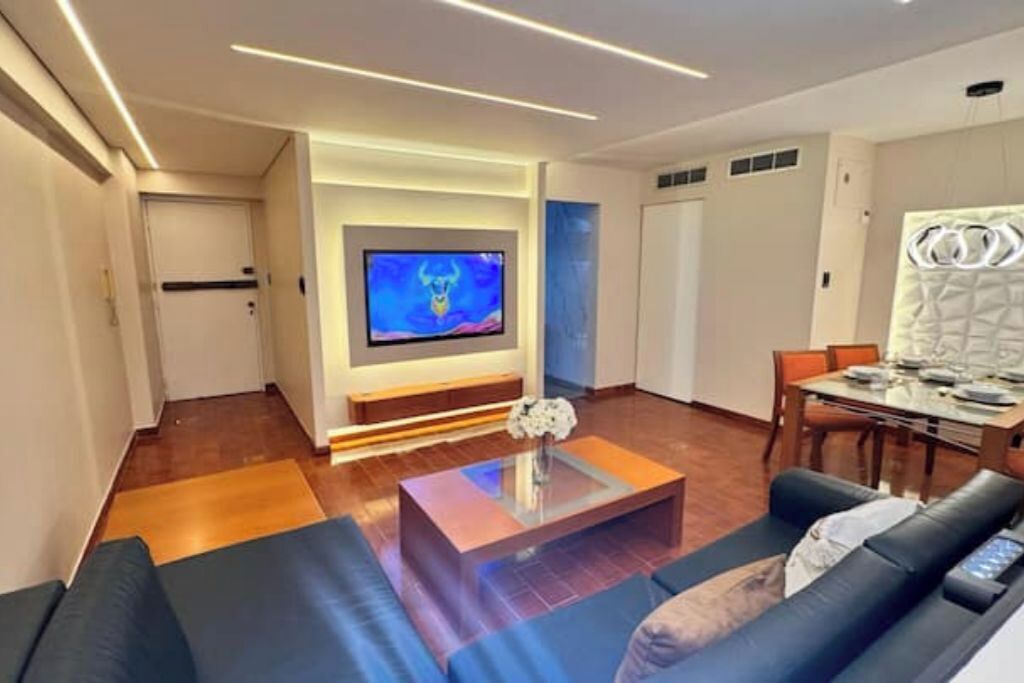 A modern living room with a flat-screen TV, a coffee table, and a dining area with a table and chairs.
