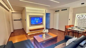 A modern living room with a flat-screen TV, a coffee table, and a dining area with a table and chairs.