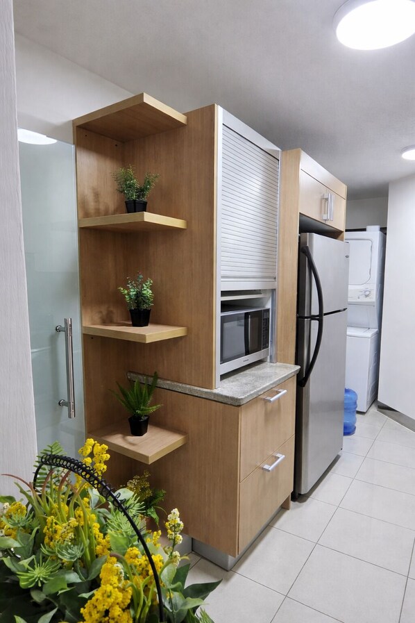 Una cocina moderna con armarios de madera, microondas integrado, refrigerador y dispensador de agua.