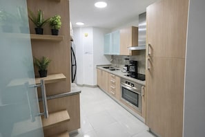 Una cocina moderna con armarios de madera, un refrigerador de acero inoxidable, un horno empotrado y una cafetera.