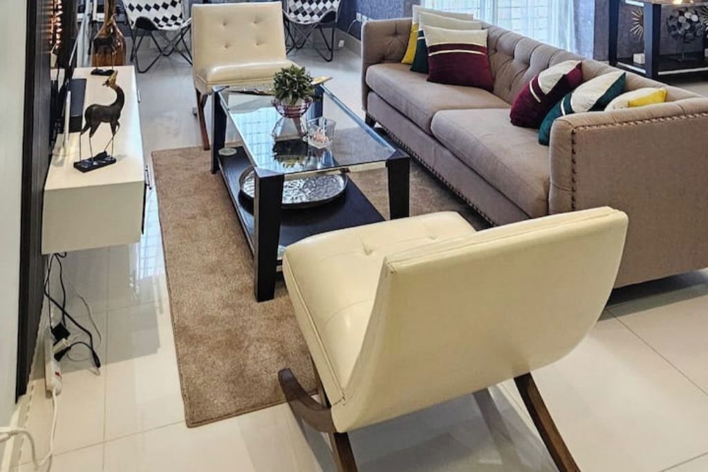 A modern living room with a beige sofa, a glass coffee table, and a white armchair.