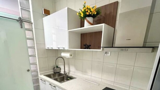 Eine Küche mit weißen Schränken, einer Edelstahl-Spüle und einem Holzboden mit einer Blumenvase.