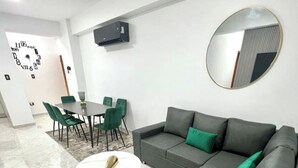 Ein modernes Wohnzimmer mit grauem Sofa, grünen Sesseln, einem runden Couchtisch und einer Wand-Klimaanlage.