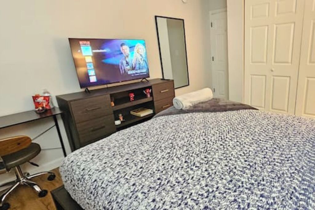 Quarto com uma cama, televisão em uma cômoda, escrivaninha e uma cadeira.