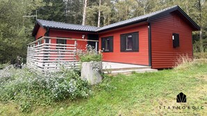 Eine rote Holzhütte mit Balkon, umgeben von viel Grün und Bäumen.