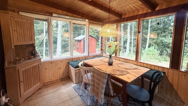 Eine Holzhütte mit Essbereich, großen Fenstern und Blick auf den Wald.