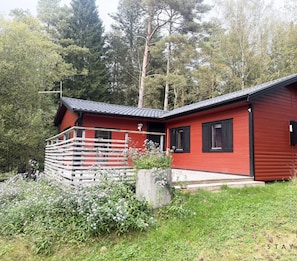 A red cabin with a balcony, surrounded by greenery and trees.
