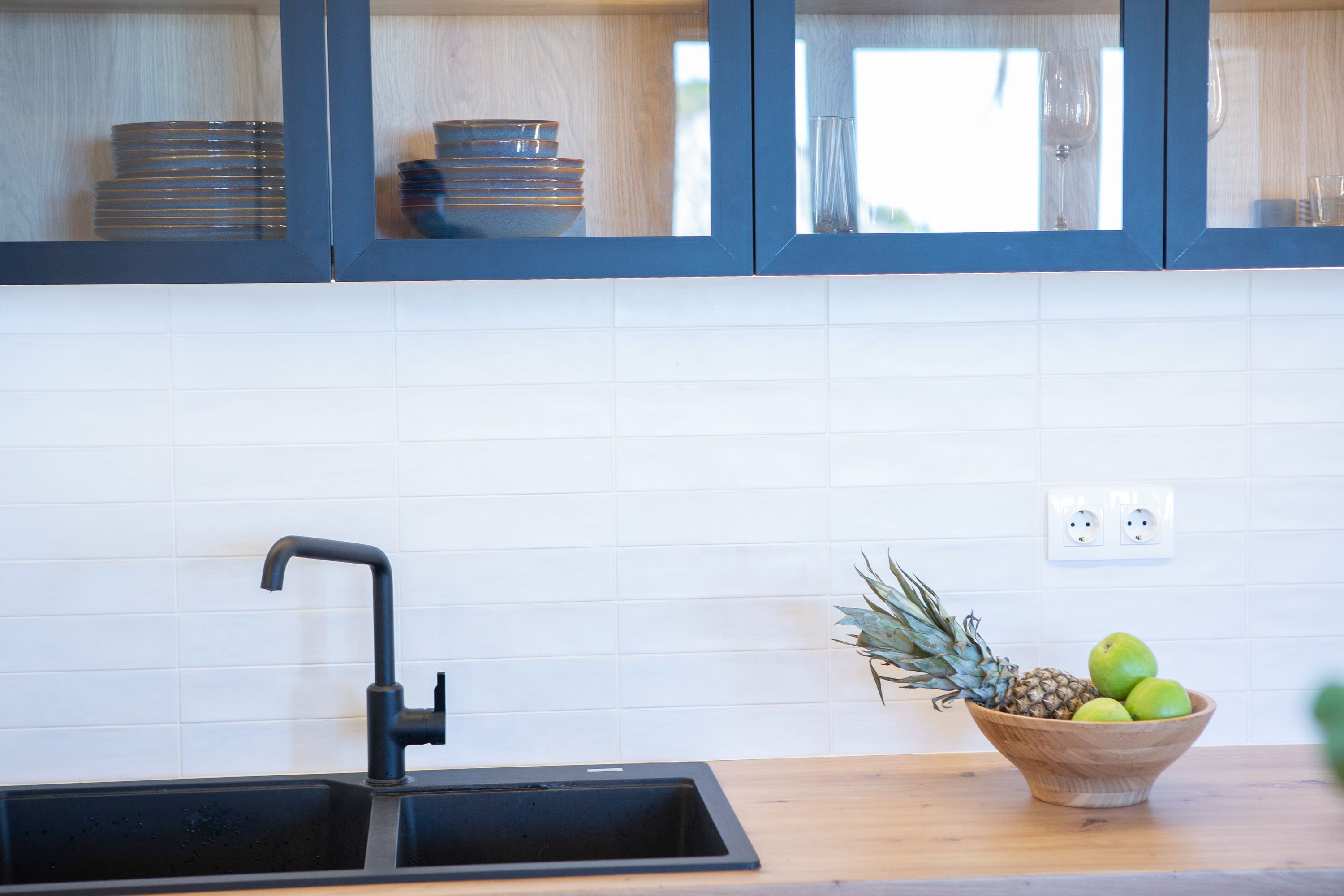 A kitchen with a black sink, wooden cabinets, and a bowl of fruit on the counter.