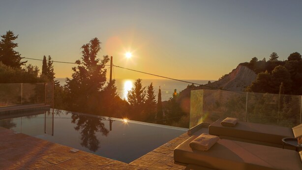 Piscina con vista sul tramonto, sedie a sdraio e cielo sereno.