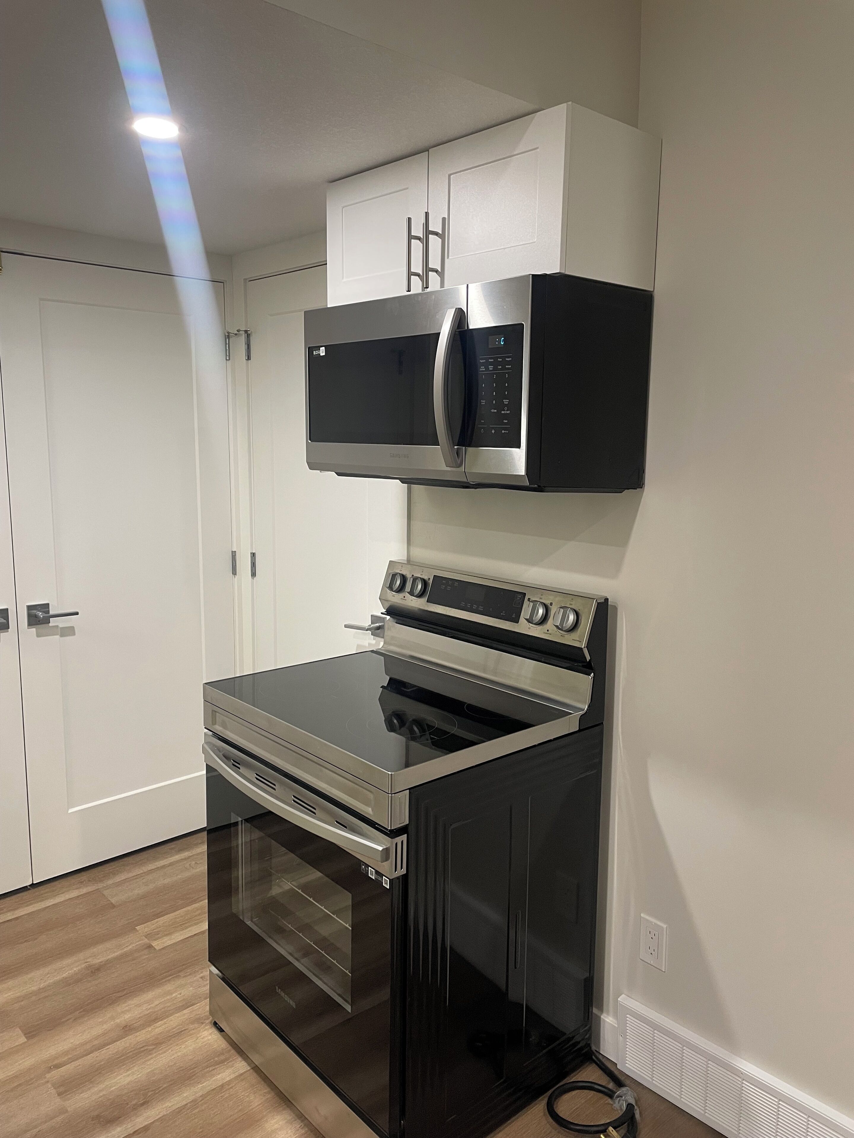 Una cocina moderna con microondas y horno integrados, armarios blancos y suelo de madera.