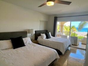 A hotel room with two beds, a ceiling fan, a nightstand with a lamp, and a balcony with a view of the ocean. - Las Mañanitas LM E3301 (San José del Cabo)