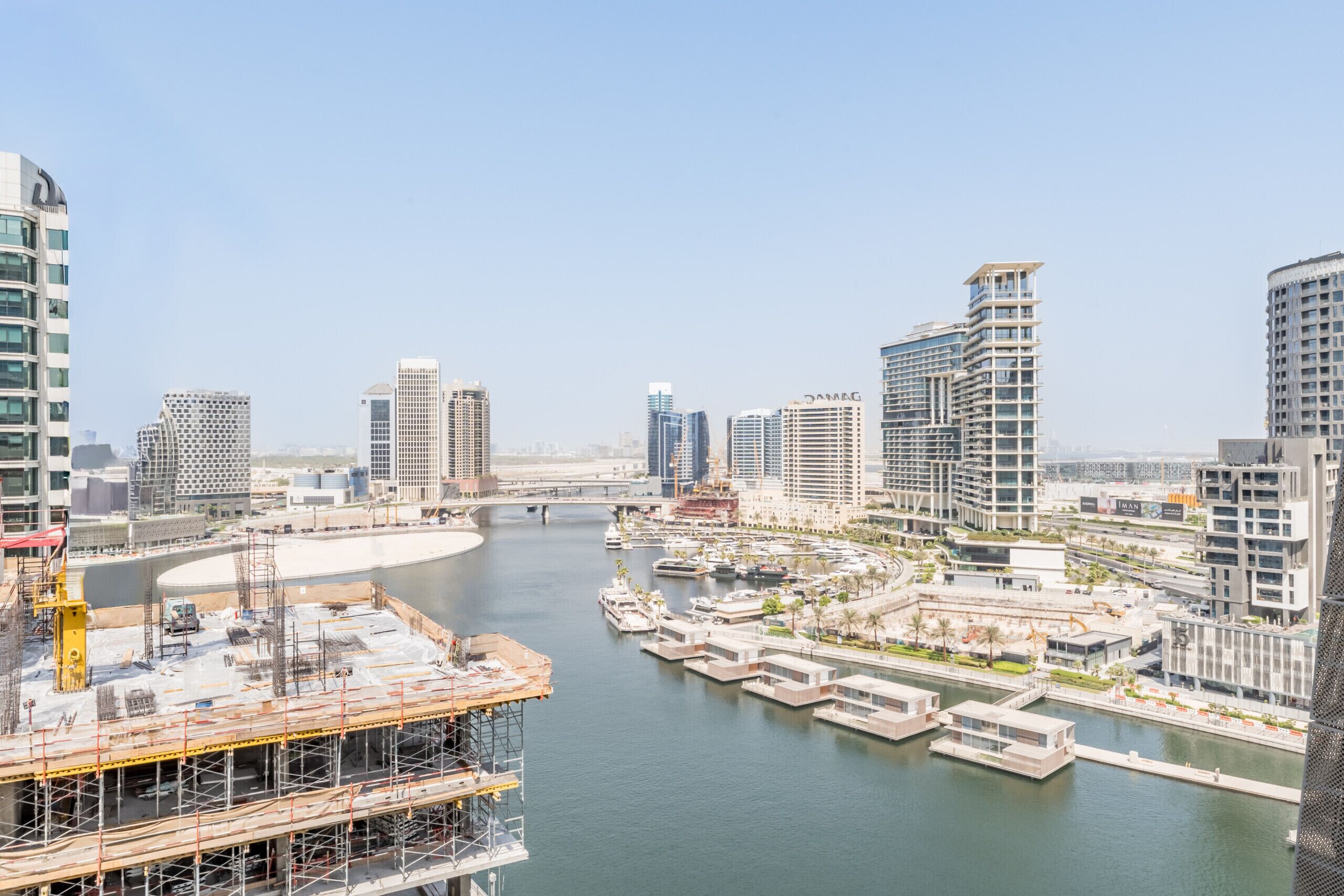 A waterfront cityscape with modern high-rise buildings, a marina, and construction sites.