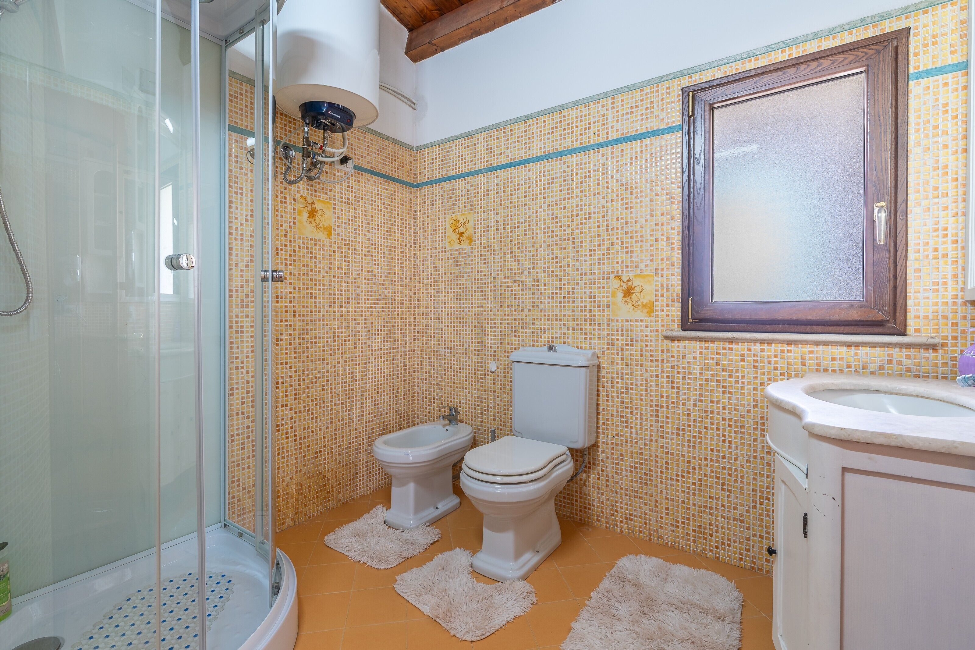 Une salle de bain avec une douche à parois de verre, deux toilettes, un lavabo et un mur recouvert de carreaux.