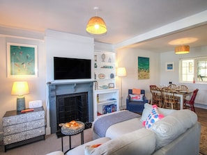 A living room with a fireplace, television, dining area, and a sofa with colorful pillows. - Rockside (Salcombe)