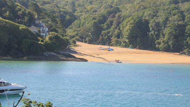 A coastal landscape with a sandy beach, a boat in the water, and a house on the left.