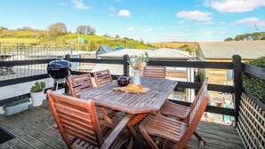 A wooden deck with a table and chairs, a barbecue grill, and a view of the countryside.