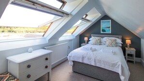 A bedroom with a skylight, a bed, bedside tables, a dresser, and a poster on the wall.