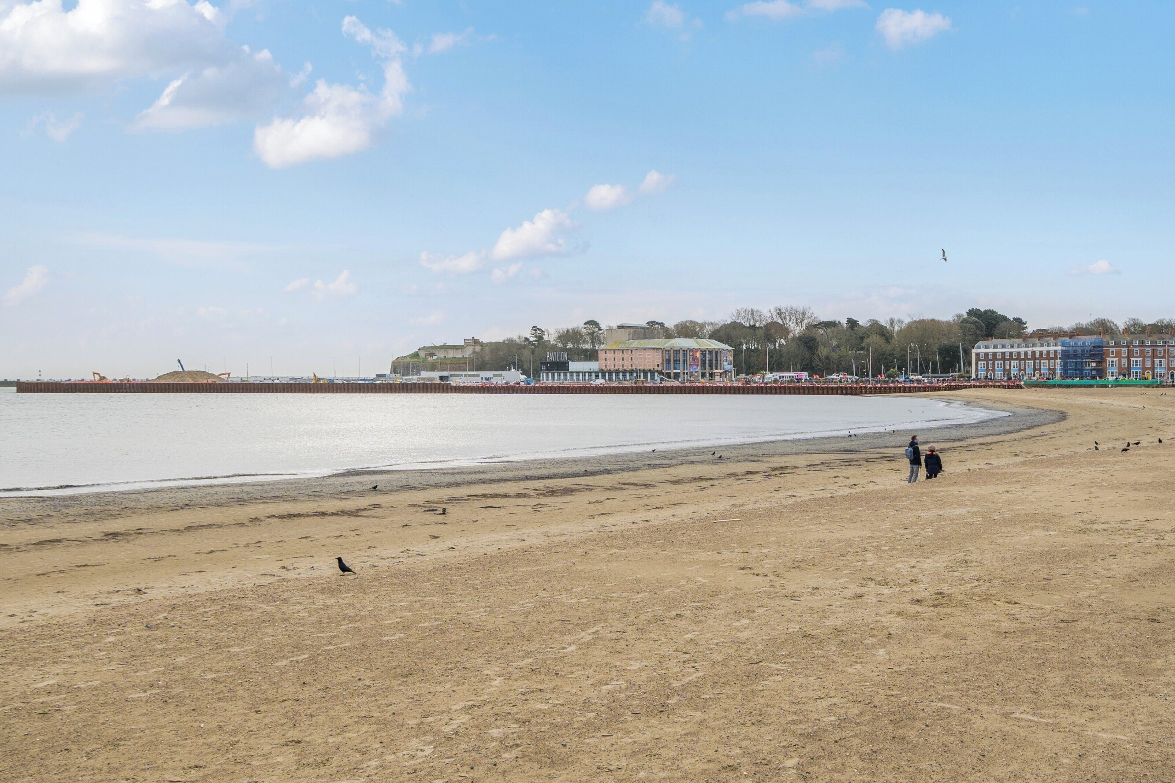 Een strand met een zandstrand, enkele personen en gebouwen op de achtergrond.