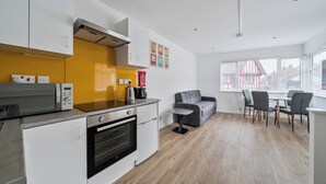 Una cocina moderna con armarios blancos, un microondas y una cafetera. Hay un sofá gris y una mesa de comedor con sillas en la sala de estar.