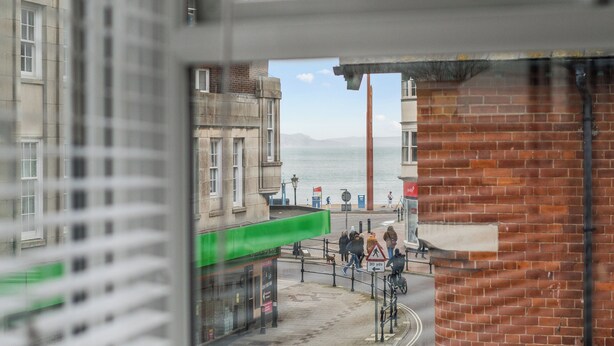 Un paisaje urbano costero con edificios, una pasarela peatonal y vistas al mar.