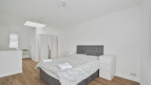 Un dormitorio con cama, mesitas de noche, armario, ventana y puerta.