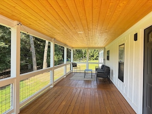 Une véranda couverte avec un plancher en bois, des rampes blanches et un espace salon comprenant une table et des chaises.