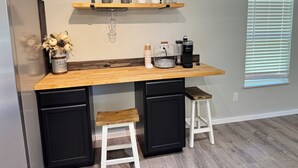 A kitchen with a wooden countertop, two stools, a coffee maker, and a shelf with mugs and glasses. - Nancy James
Charming 2-bedroom retreat with a charming porch in Candler (Candler)
