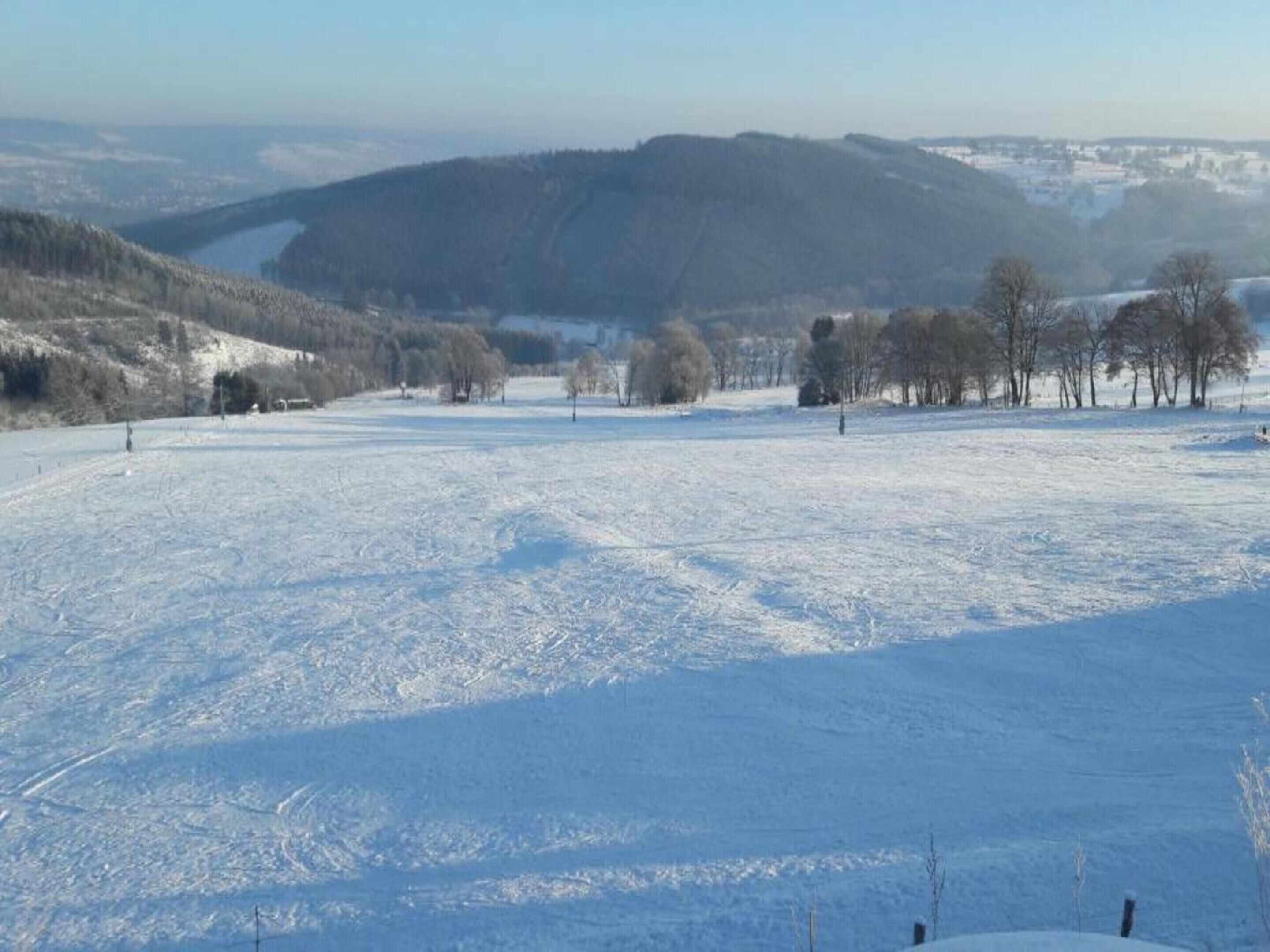 A snow-covered landscape with a valley and distant hills.