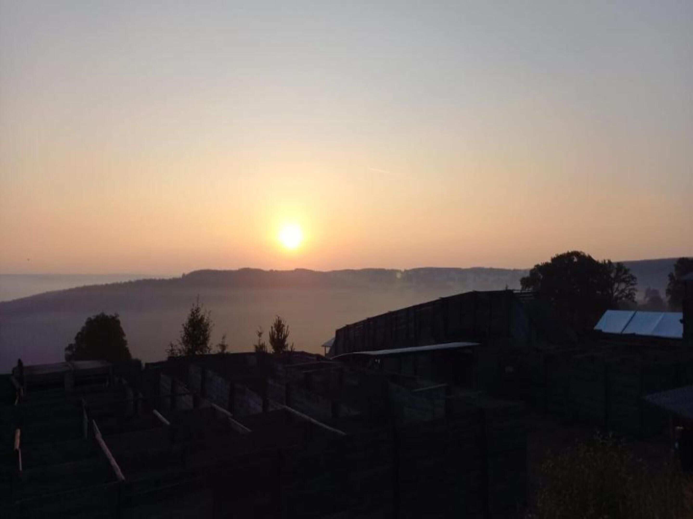 A sunrise over a hilly landscape with buildings in the foreground.
