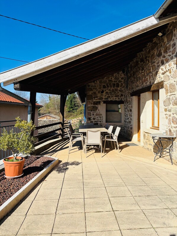 Une terrasse avec un mur en pierre, un espace salon abrité et une plante en pot.