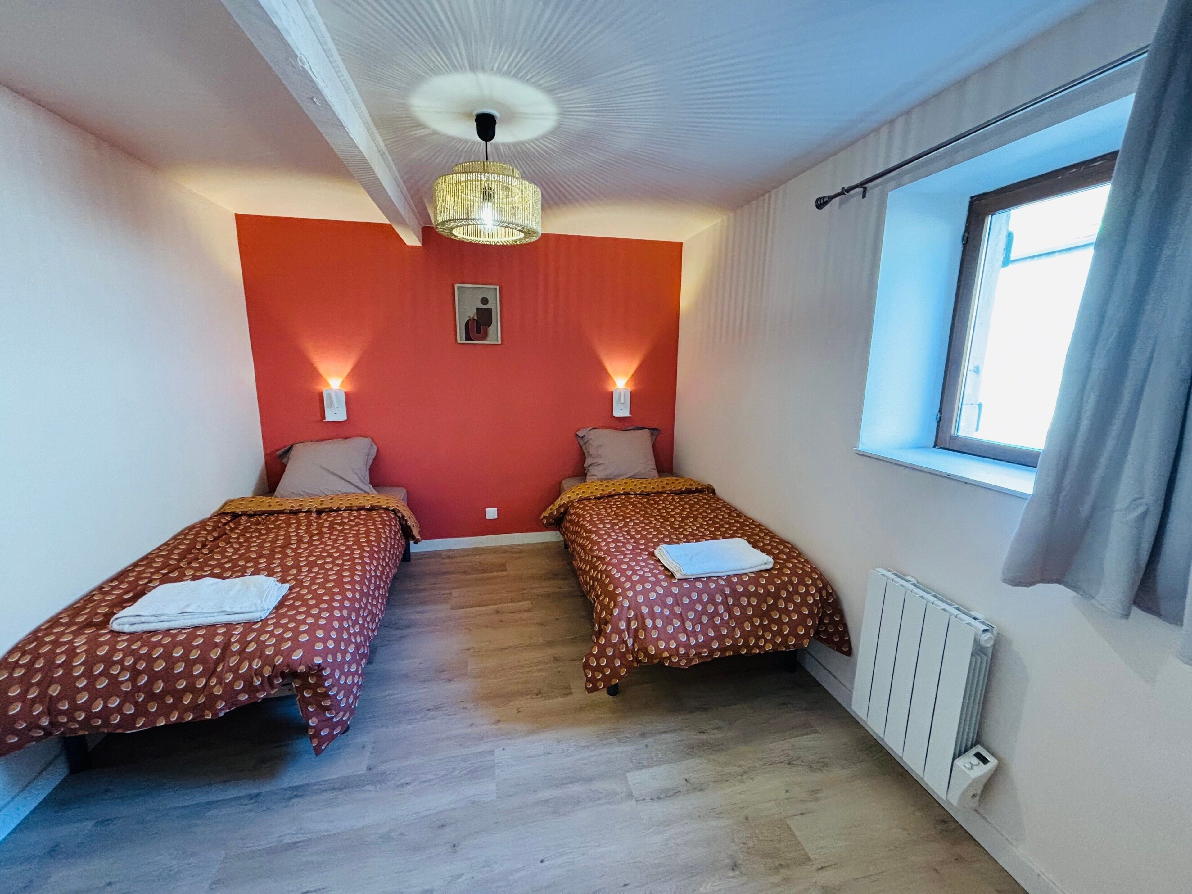A room with two single beds, a ceiling fan, a radiator, and a window with curtains.