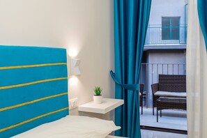 Une chambre d’hôtel avec un lit, une petite table avec une plante, une fenêtre avec des rideaux et un balcon avec une chaise.