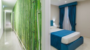 A hotel room with a bed, a nightstand, a lamp, and a wall with a green bamboo design.